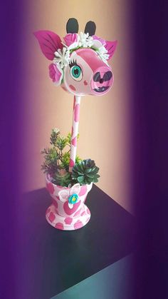 a pink giraffe planter with flowers in it on a black table next to a purple wall