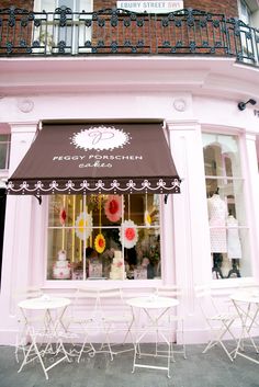 a pink store front with tables and chairs in front of the window that has a cake shop sign above it