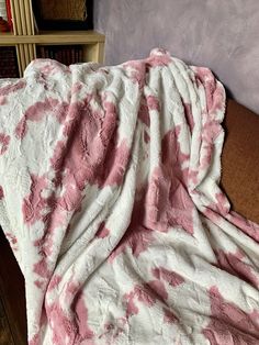 a pink and white blanket sitting on top of a couch next to a book shelf