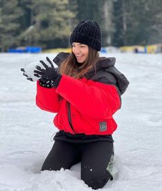 a woman sitting in the snow with her hands up to her chest and smiling at the camera