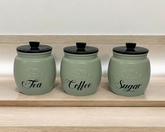 three green canisters with black lids on a wooden shelf