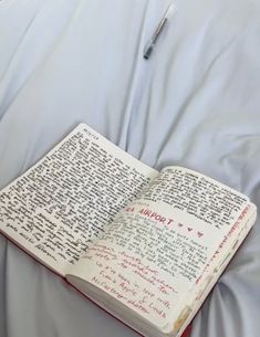 an open book sitting on top of a bed covered in white sheets with writing on it