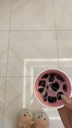 a person holding a cup filled with liquid on top of a tiled floor next to a stuffed animal