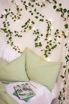 a bed topped with pillows covered in green leaves and string lights next to a white headboard