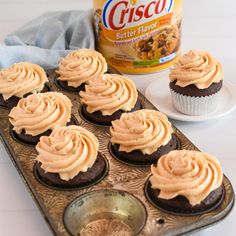 cupcakes with frosting in a muffin tin next to a can of bisco butter flavor