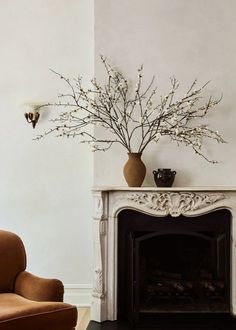 a living room with a fire place, chair and vase on top of the fireplace