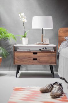 a bedroom with a bed, nightstand and plant on the side table in front of it