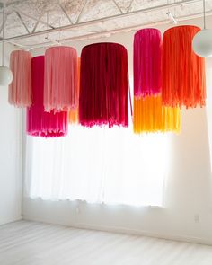 several different colored lamps hanging from the ceiling in front of a window with white curtains