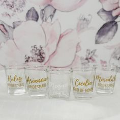 four shot glasses sitting on top of a table next to a flowered wallpaper