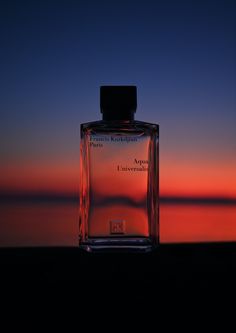 a bottle of perfume sitting on top of a table next to the ocean at sunset