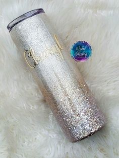 a silver glitter tumbler sitting on top of a white fur covered floor next to a blue and purple sticker