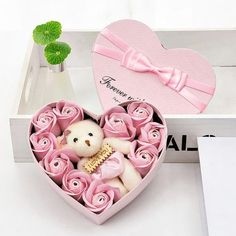 a small teddy bear in a heart shaped box with pink roses and a bow tie