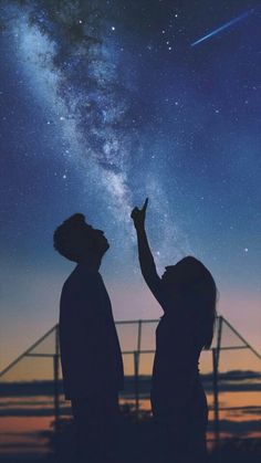 two people are looking up at the stars in the sky with their hands raised to the night sky