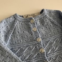 a knitted sweater with buttons on the front and back, sitting on a table