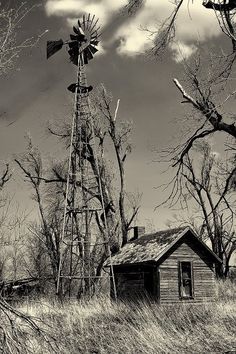 black and white photograph of an old farm house with a windmill in the foreground