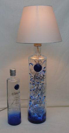 a glass bottle with blue liquid in it next to a lamp on a white surface