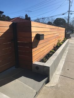 a wooden fence is next to a concrete planter on the side of a street