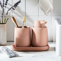 three toothbrushes and two toothpaste holders on a counter with lavenders in the background