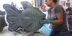 a woman is working on a statue of a fish