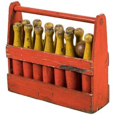 an old red wooden box filled with yellow and brown bowling pins on top of each other