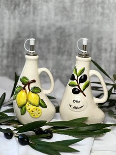 two vases with lemons painted on them sitting next to leaves and olives