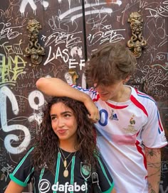 two young people standing next to each other in front of graffiti covered wall and door