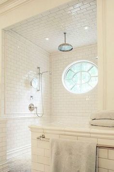 a bathroom with white tiles and a round window in the shower area, along with two towels on the counter