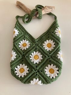 a green crocheted purse with white and yellow flowers hanging from it's side