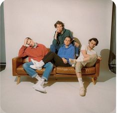 three men sitting on a couch in front of a white wall and one man is holding his hand up to his ear