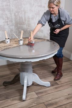 a woman painting a table with paintbrushes on it