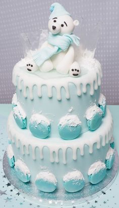 a blue and white frosted cake with a teddy bear sitting on top of it