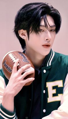 a young man holding a football in his right hand and wearing a green varsity jacket