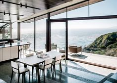 an open kitchen and dining area overlooks the ocean from inside a modern home with glass walls