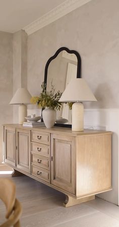 a large mirror sitting on top of a wooden dresser next to a table with two lamps