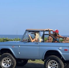 three women sitting in the back of a pick up truck with surfboards on top