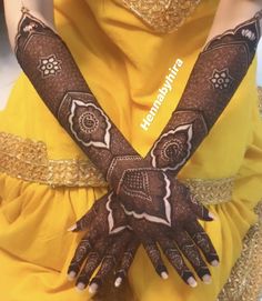 a woman in yellow dress holding her hands up with henna tattoos on it's arms