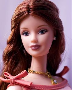 a close up of a doll wearing a pink dress with a gold chain around it's neck