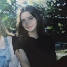 two women standing next to each other with trees in the background