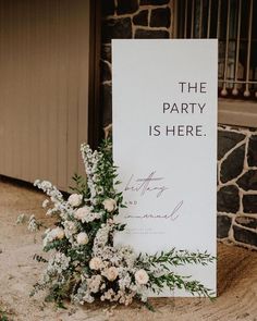 a sign that says the party is here next to flowers and greenery in front of a stone wall