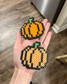 two pieces of perler bead art that look like pumpkins on the palm of someone's hand