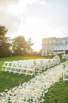 an outdoor ceremony with white chairs and flower petals on the grass in front of a large building