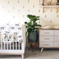 a baby crib next to a dresser with a potted plant