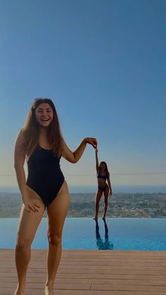 two women in swimsuits standing near a swimming pool and posing for the camera