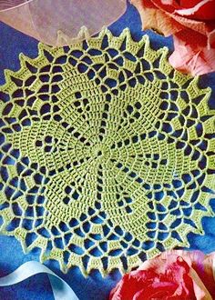 a crocheted doily is laying on a blue table cloth with flowers in the background