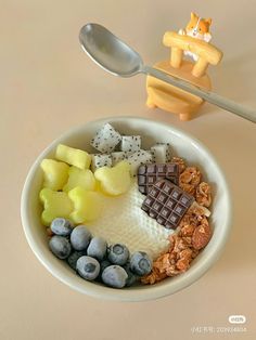 a bowl filled with cereal, nuts and other foods next to a spoon on top of a table