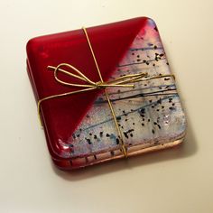 a red box wrapped in gold string and tied with a bow sitting on top of a white table