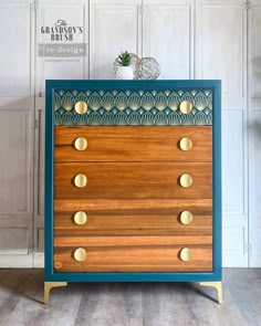 a blue and wooden dresser with brass knobs on it's sides, against a white wall