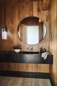 a bathroom with wood paneling and a round mirror on the wall above the sink