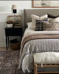 a bed with pillows and blankets on top of it next to a night stand in front of a painting