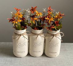 three mason jars with flowers in them on a table